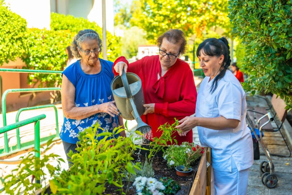 Two senior women and nurse watering plants in the garden of geriatrics facility